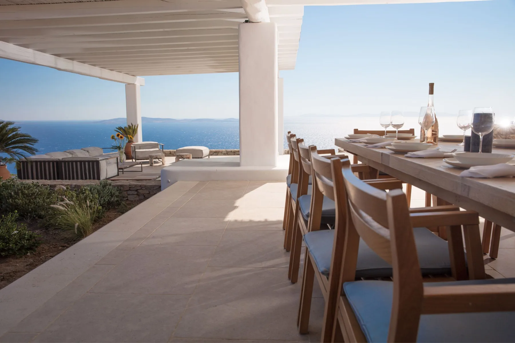 A seaside terrace has a dining table and seating beneath a covered patio.