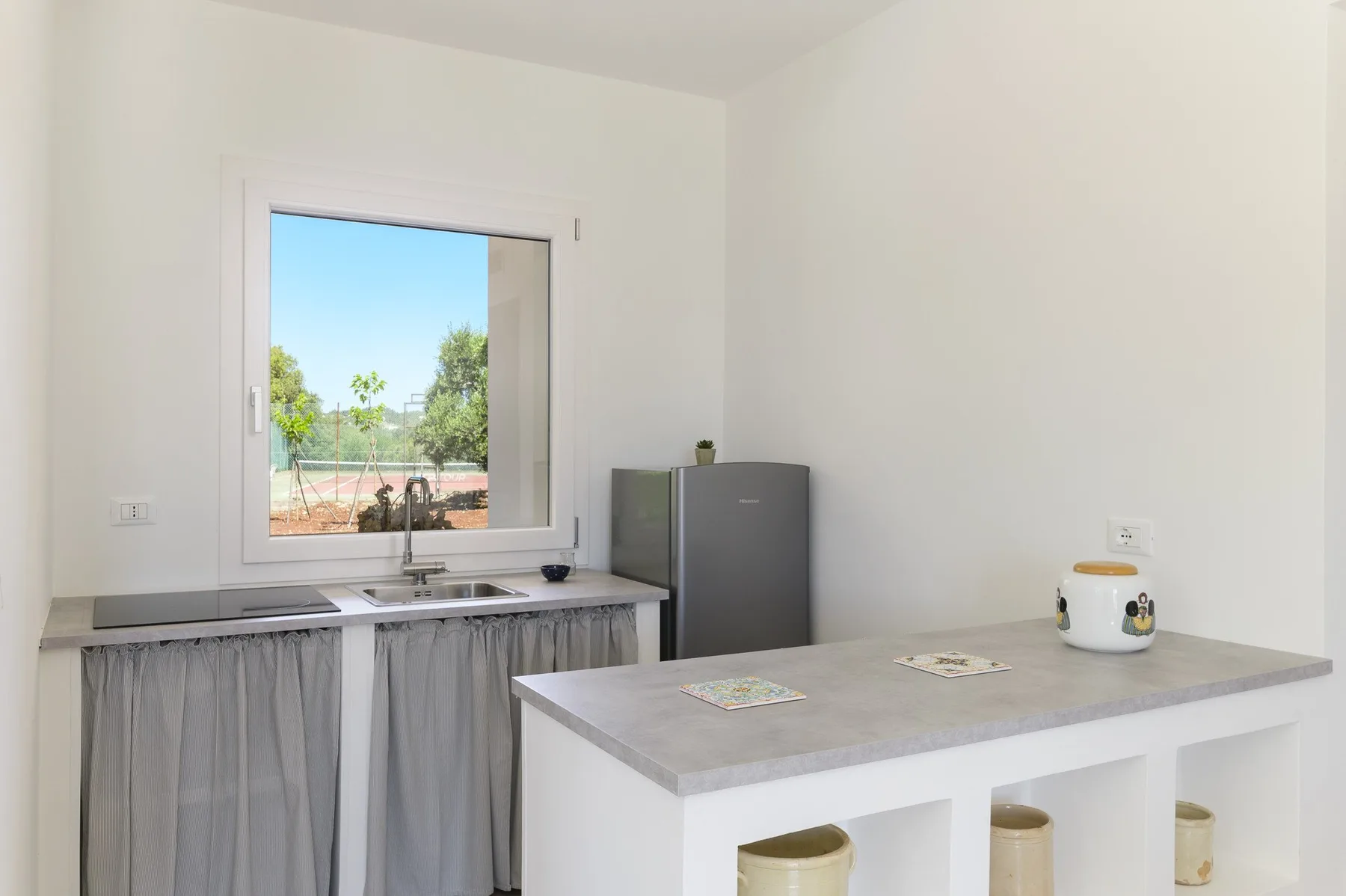 Una cocina luminosa con un fregadero bajo una ventana y una encimera central.