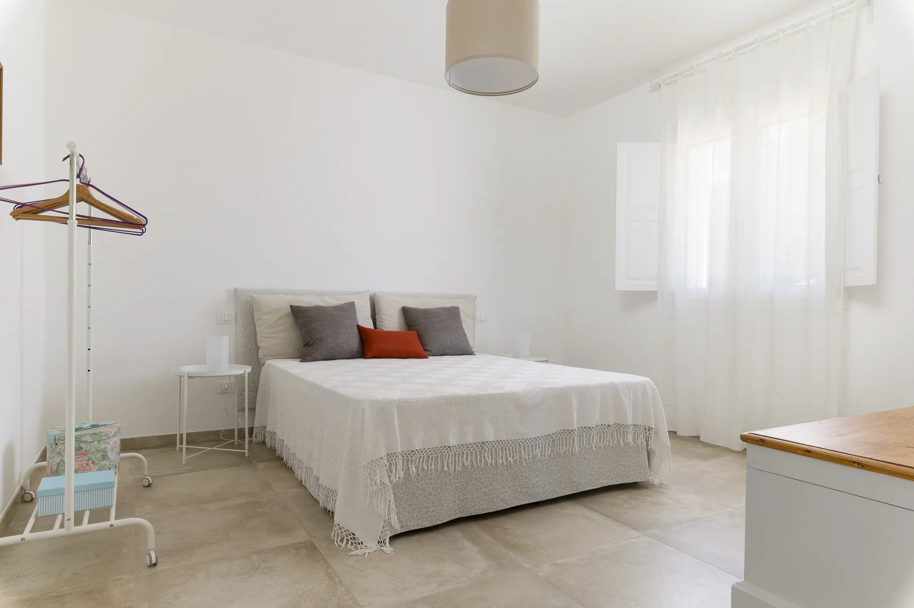 A bright bedroom with a neatly made bed and a sunlit window.