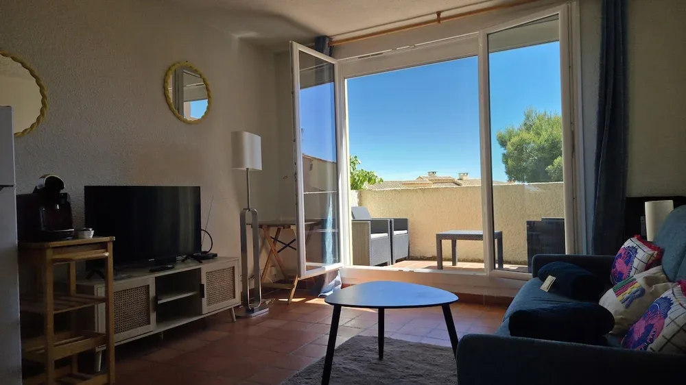 A living room with seating and a coffee table beside open glass doors.