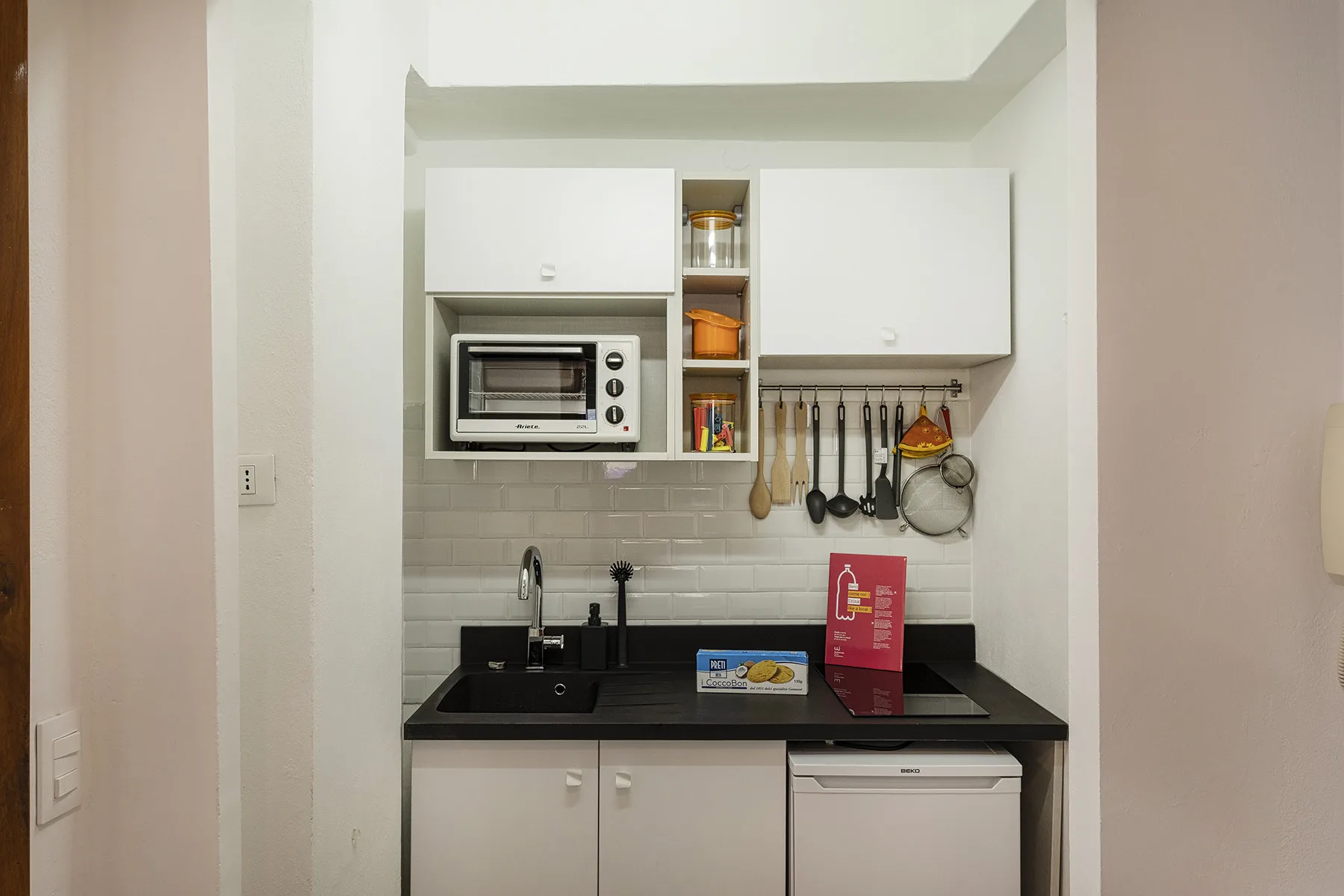 Una cocina compacta con gabinetes blancos, una encimera negra y utensilios de cocina.