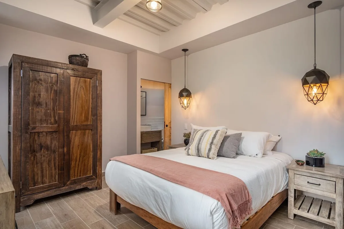 Dormitorio con una cama, un armario de madera y lámparas colgantes.
