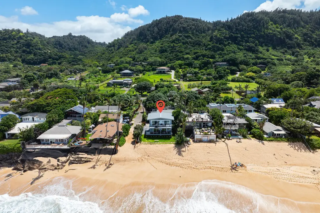 Vista aérea de casas frente a la playa, junto a una costa arenosa y colinas verdes.