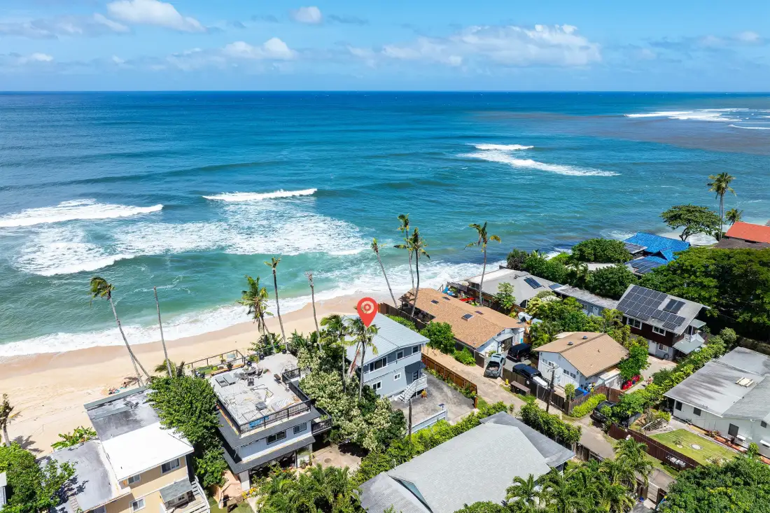 Vista aérea de una costa tropical con olas y edificios junto a la playa.