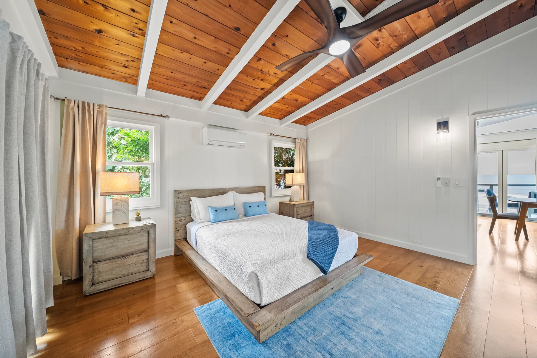 Un dormitorio luminoso con una cama bajo un techo de madera y vigas blancas.