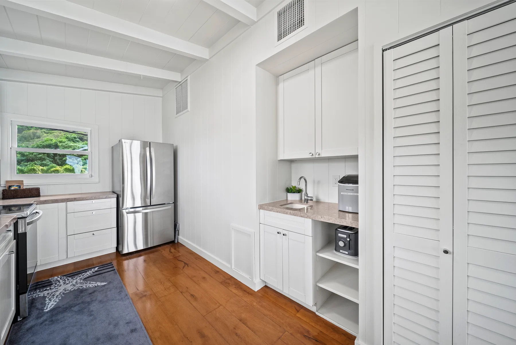 Una cocina luminosa con gabinetes blancos, un refrigerador y piso de madera.