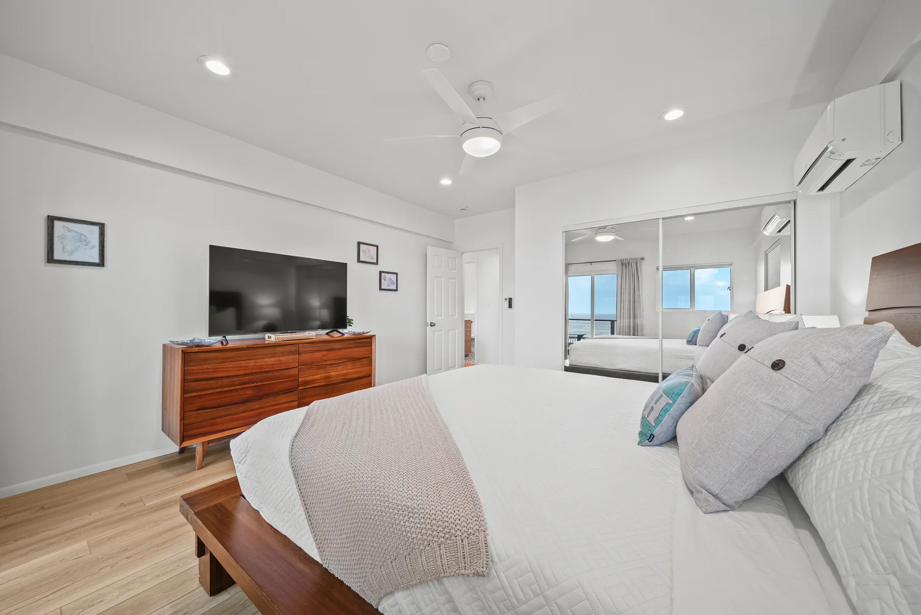 Un dormitorio luminoso con una cama grande, una cómoda de madera y puertas de armario espejadas.