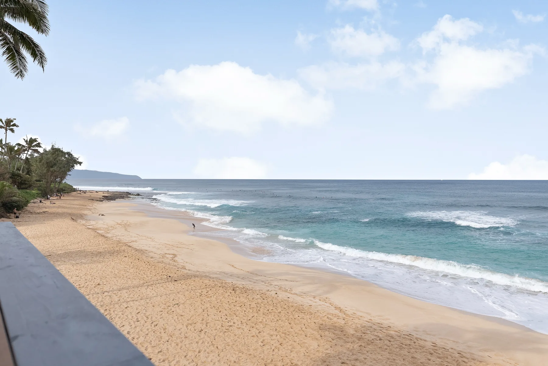 Una playa de arena bordea olas turquesas bajo un cielo parcialmente nublado.