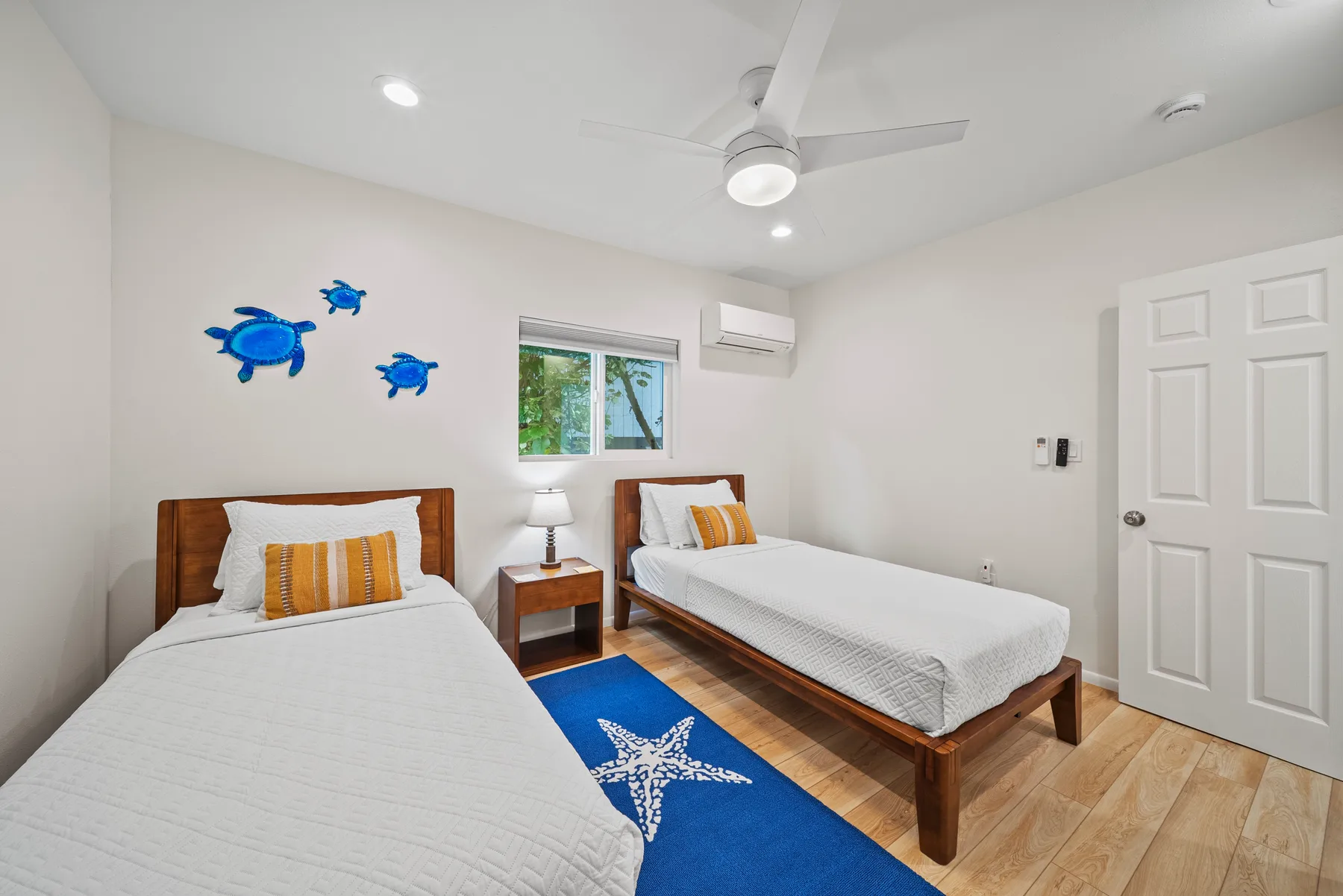 Un dormitorio luminoso con dos camas, una alfombra azul y adornos en la pared.