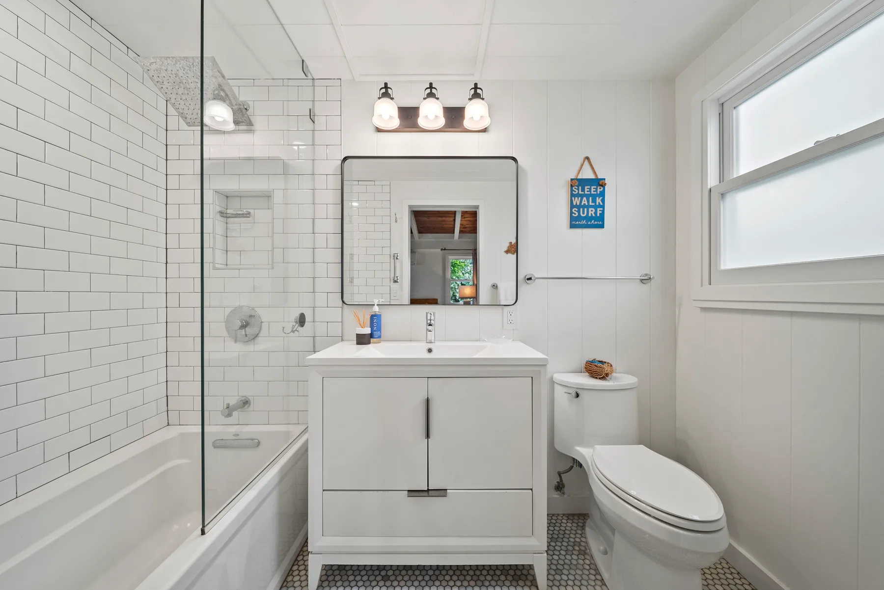 Un baño luminoso con tocador, espejo y ducha con panel de vidrio.