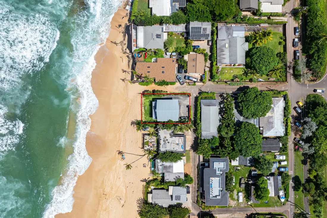 Una vista aérea muestra una playa de arena junto a las olas y casas cercanas.
