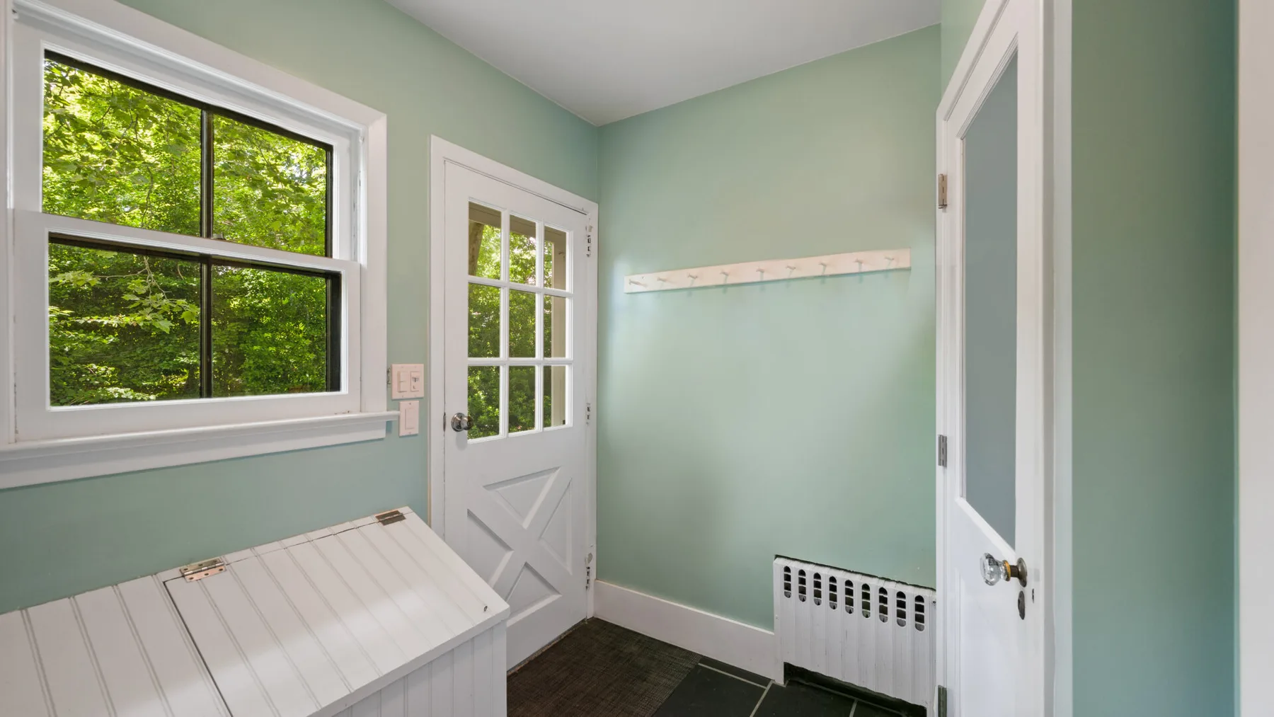 A pale green entryway with a window, a white door, and a wall-mounted coat rack.