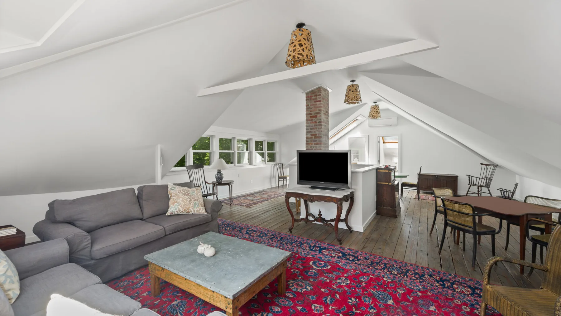 A bright attic living and dining area with seating, tables, and sloped ceilings.