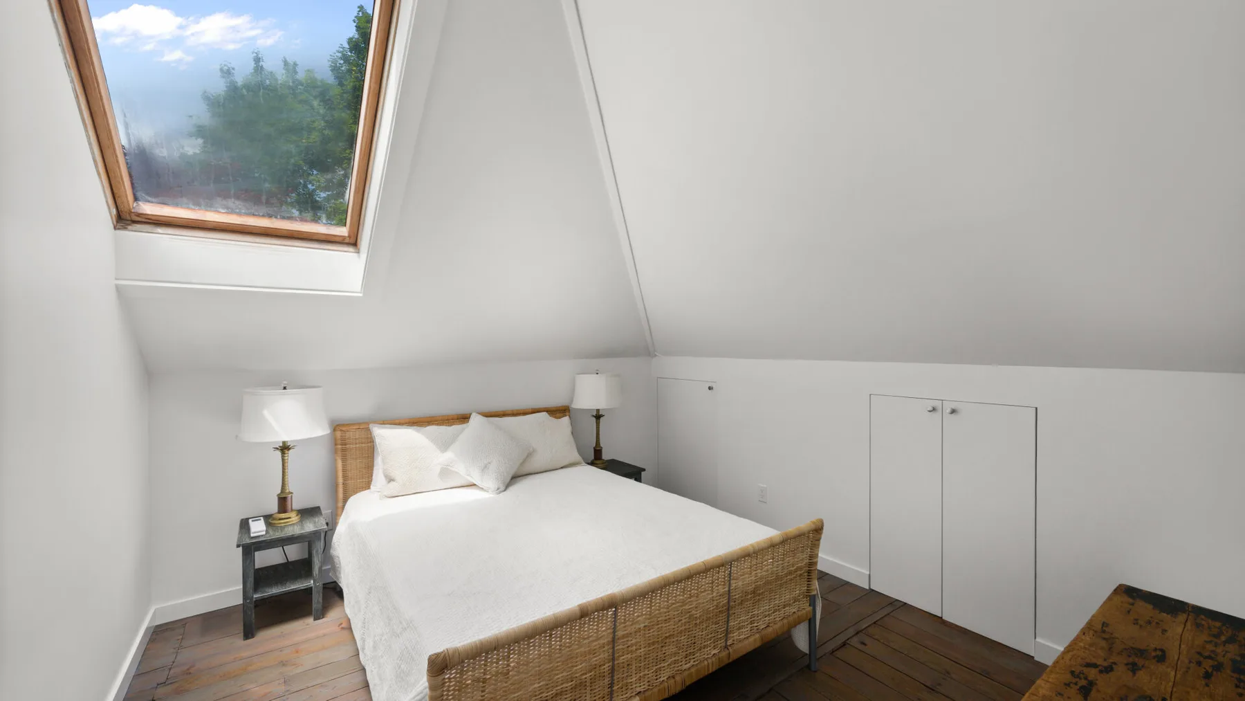 A bedroom with a bed beneath a sloped ceiling and a skylight.