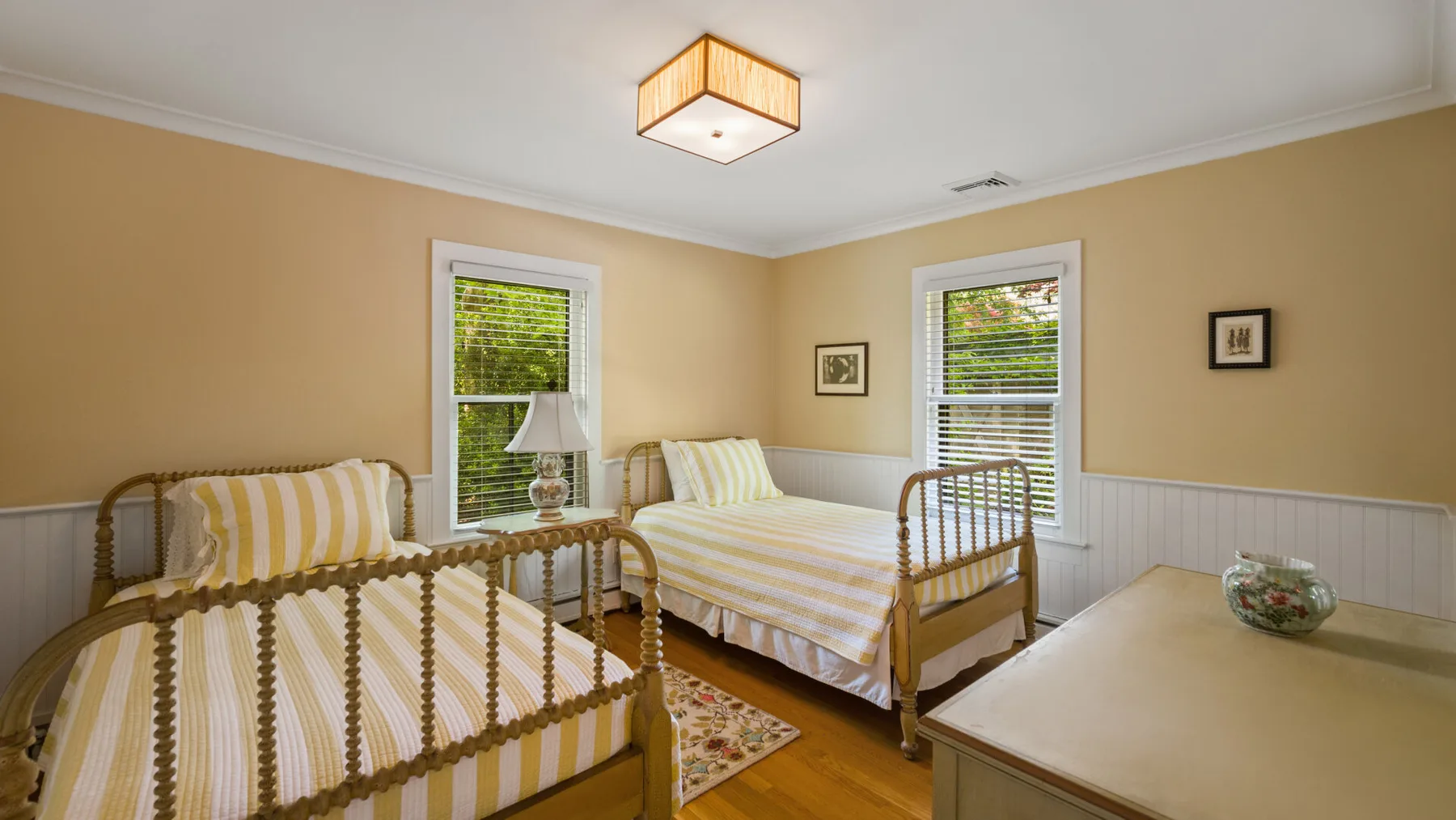 A bedroom with striped bedding, two beds, and windows overlooking greenery.