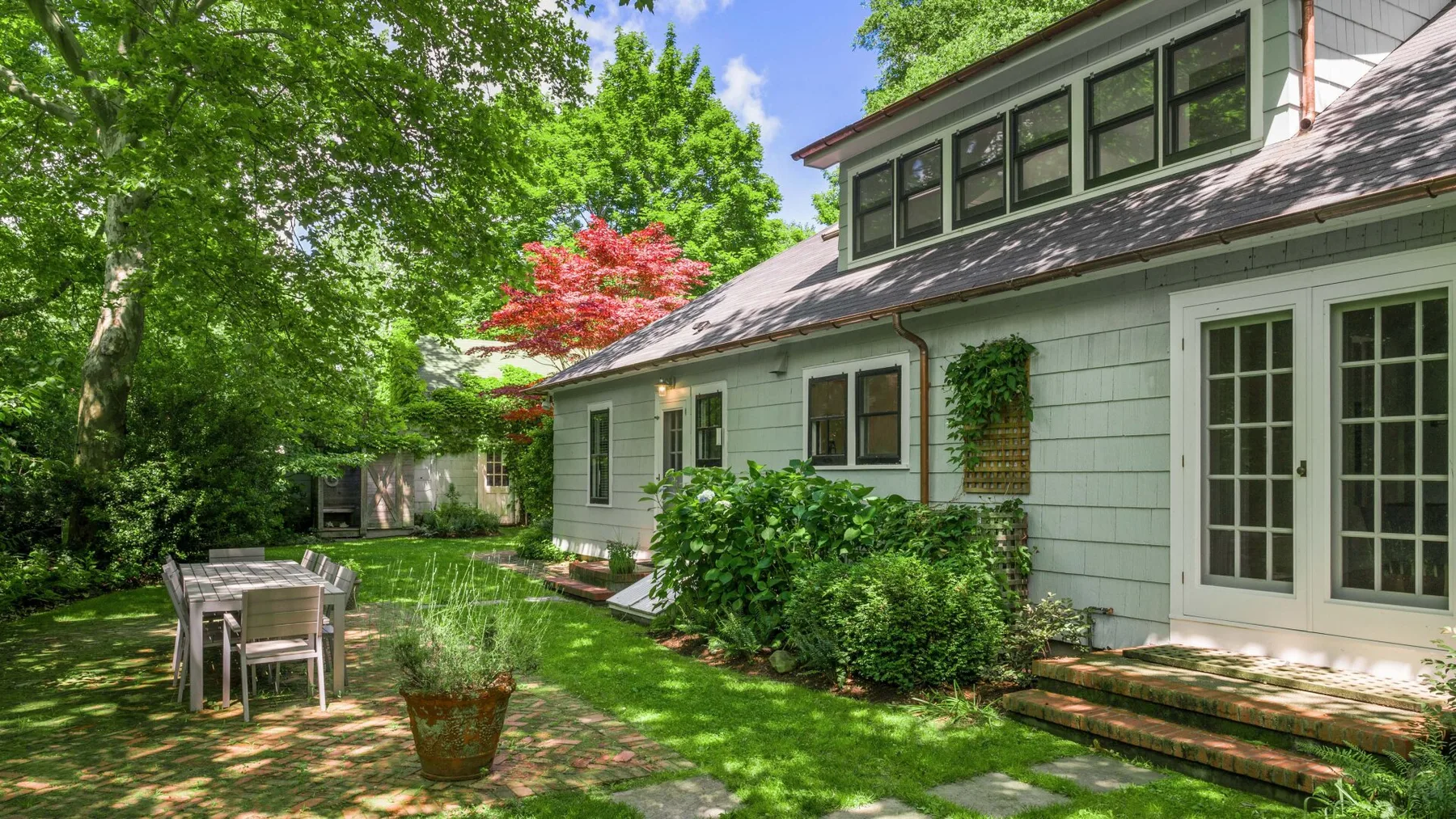 A leafy garden patio beside a pale green house with a small outdoor table.