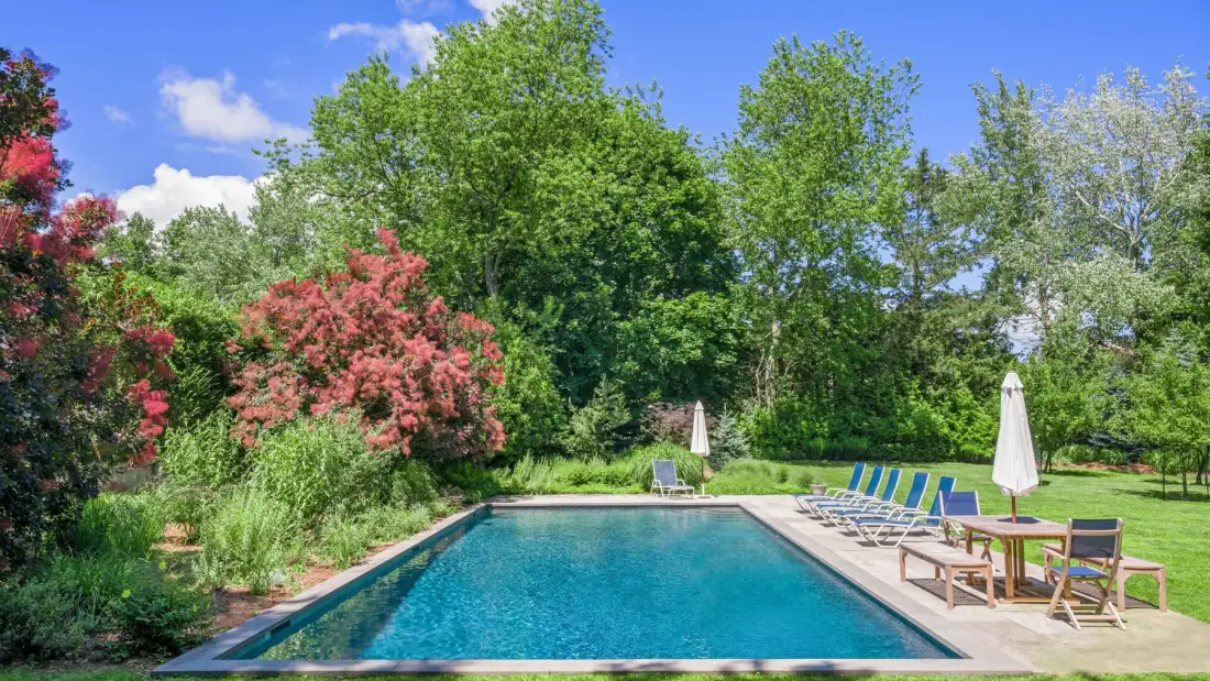 An outdoor swimming pool sits beside patio seating and garden greenery.