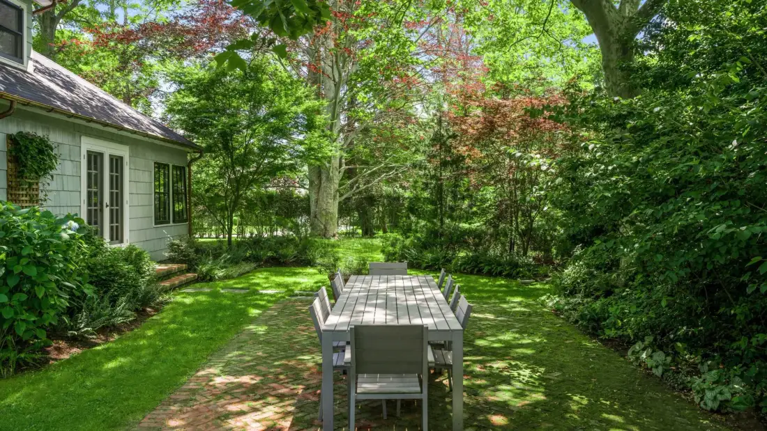 A garden patio with an outdoor dining table surrounded by trees and greenery.