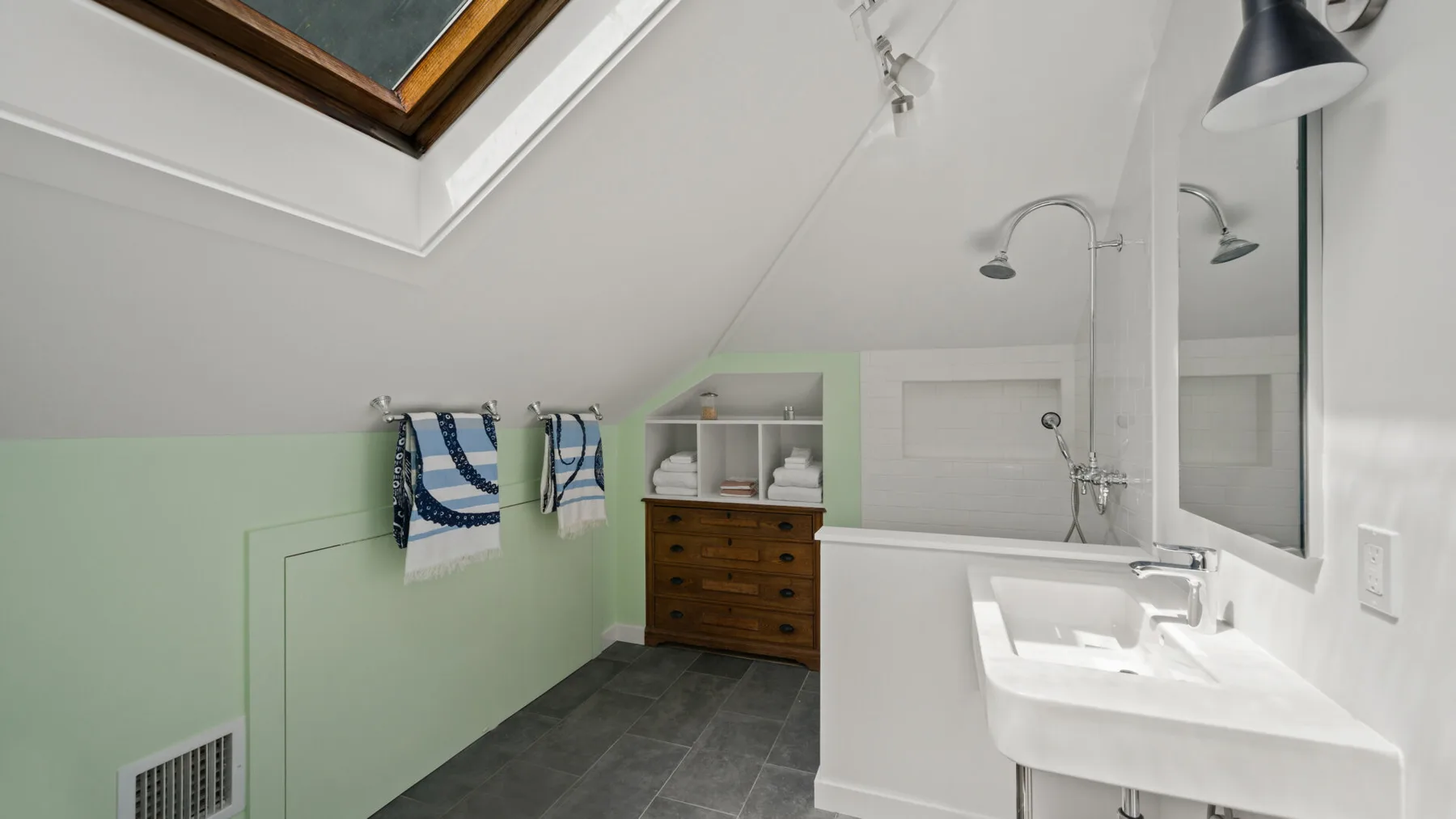 A sloped-ceiling bathroom with a sink, shower, and wooden vanity.
