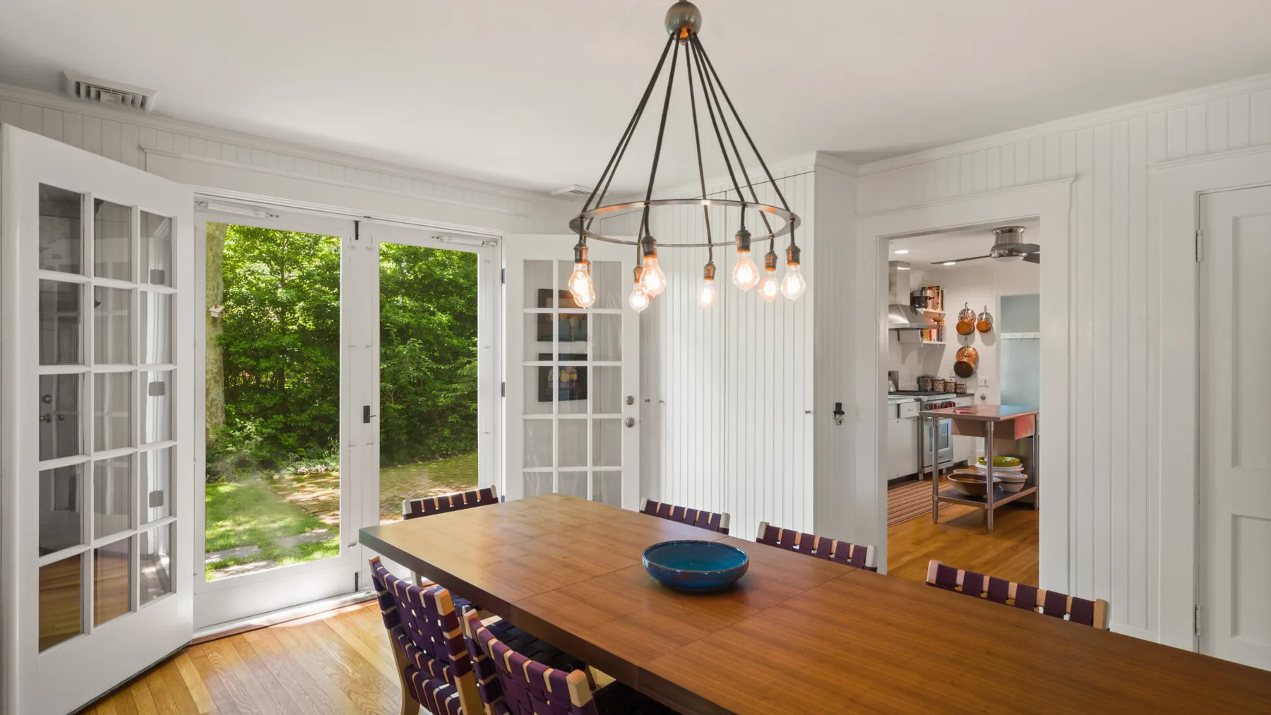 A bright dining room with a long wooden table and glass doors opening to greenery.