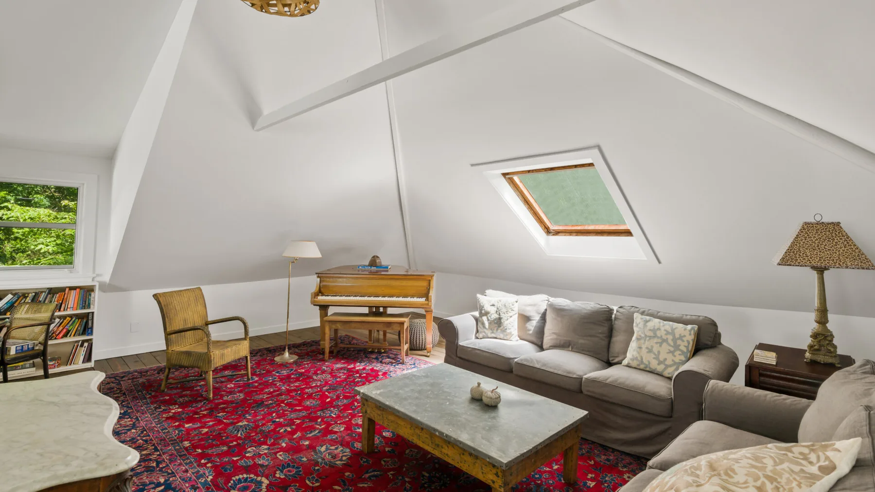 A bright attic sitting room with seating around a coffee table on a patterned rug.