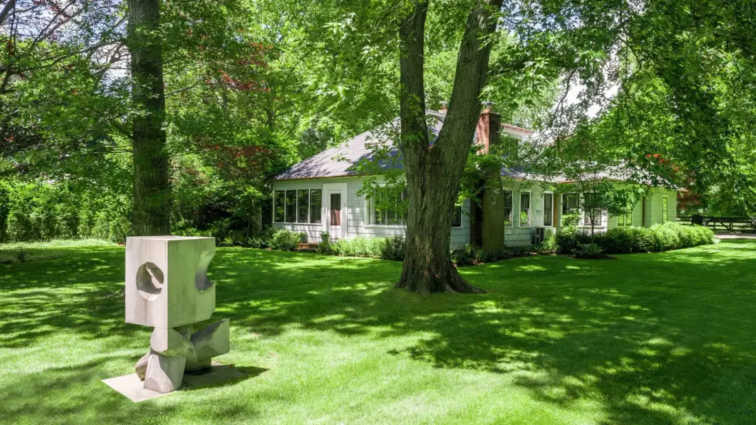 A white house sits among leafy trees beside a broad green lawn.