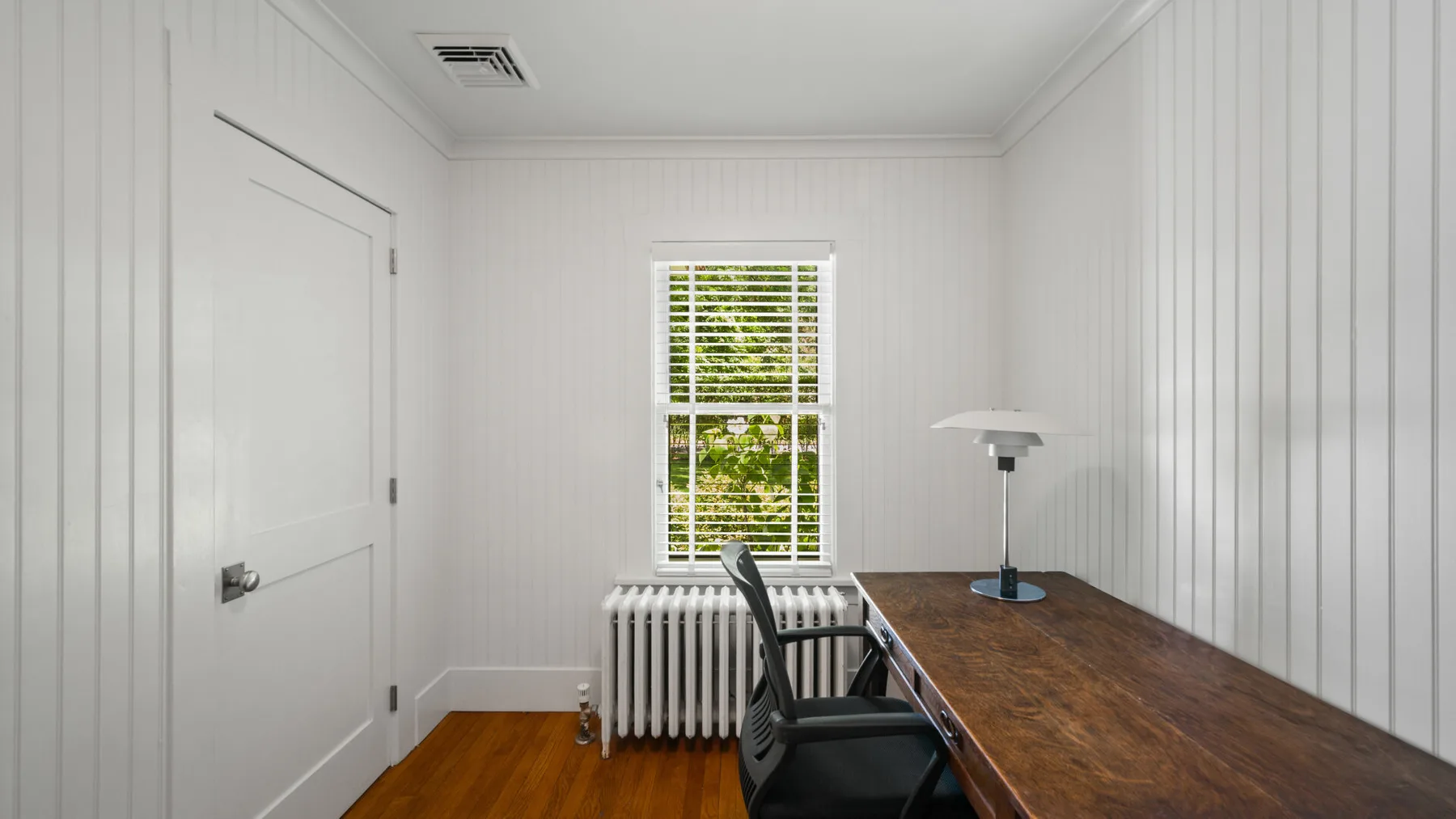 A small room with a long wooden desk, a chair, and a window.
