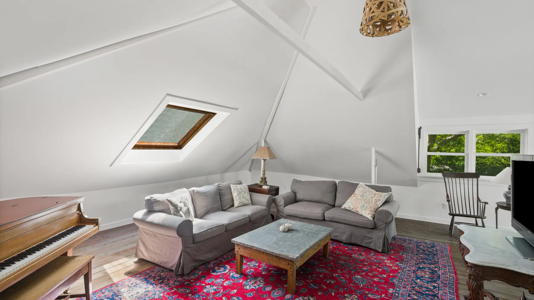 A bright living room with sectional seating, a coffee table, and a piano.