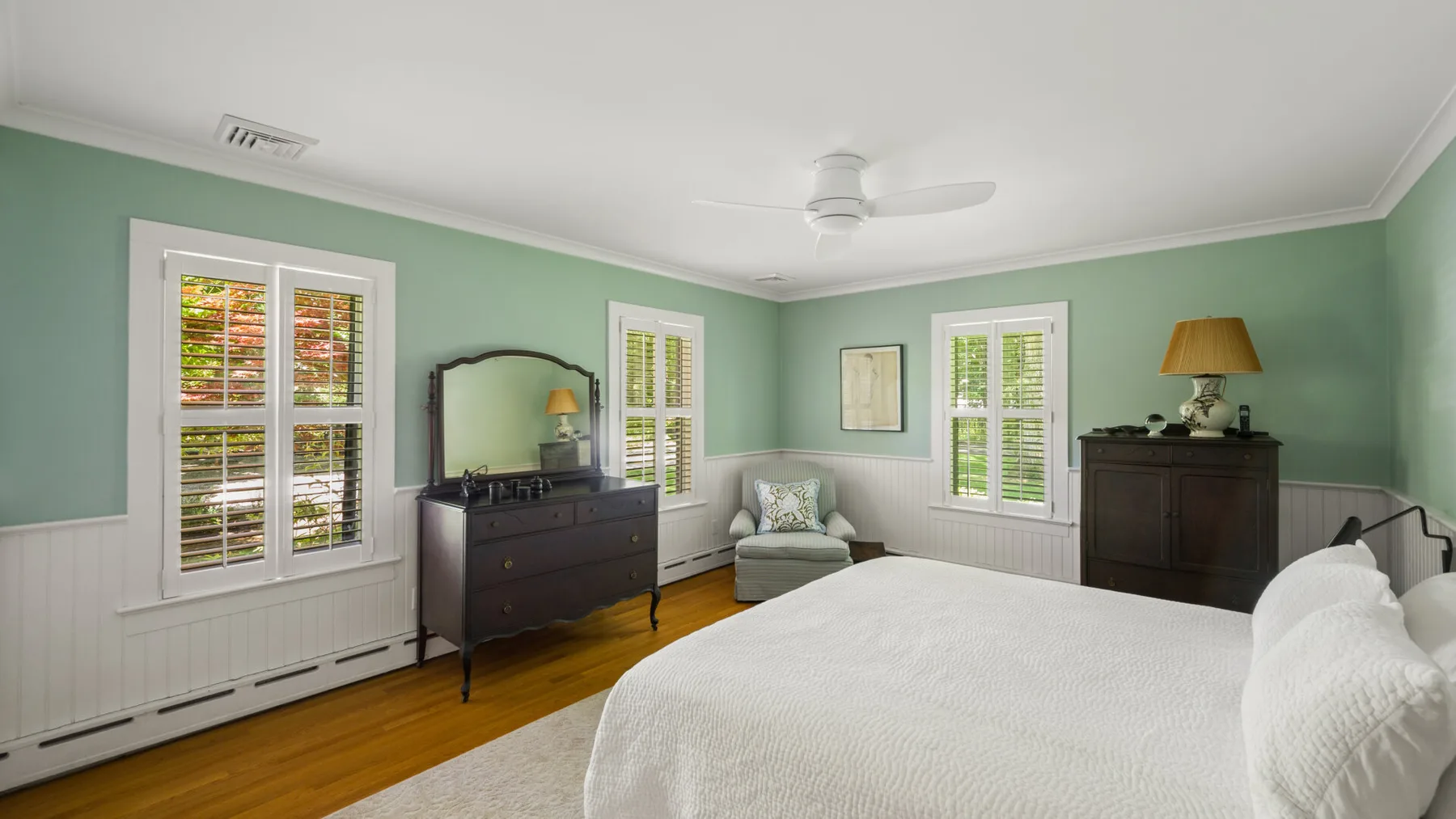 A bright bedroom with a neatly made bed, green walls, and several windows.