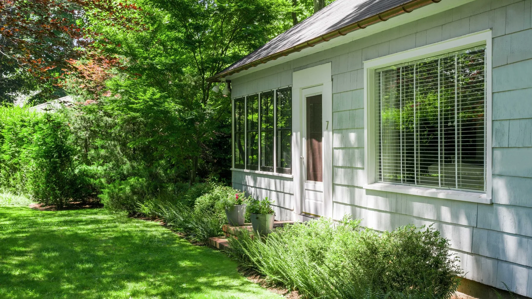 A white house exterior bordered by a green lawn and leafy shrubs.