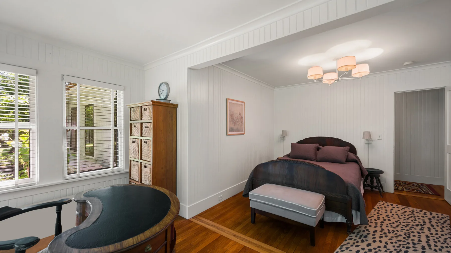 A bedroom with a bed, a small table, and windows along one wall.