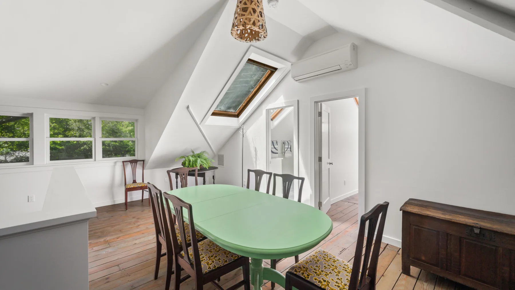 A dining area with a green table and several chairs beneath a sloped ceiling.