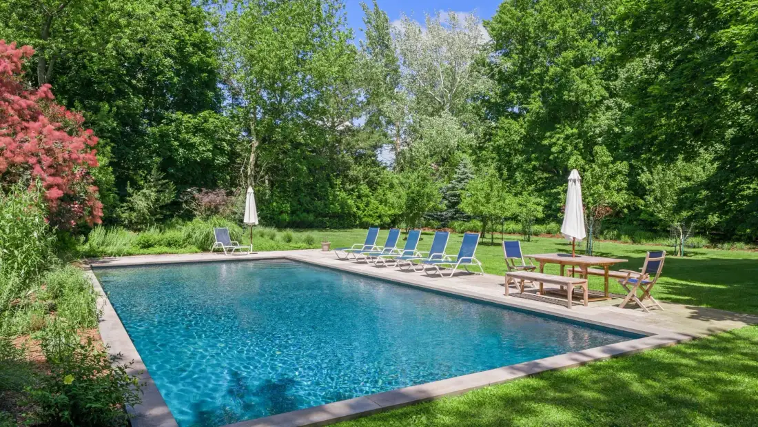 An outdoor swimming pool is surrounded by trees and lounge seating.