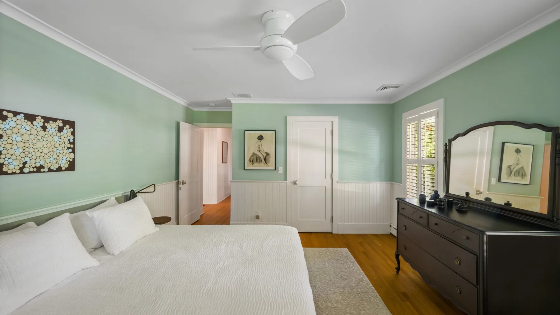 A bedroom with a large bed, dresser, and pale green walls.