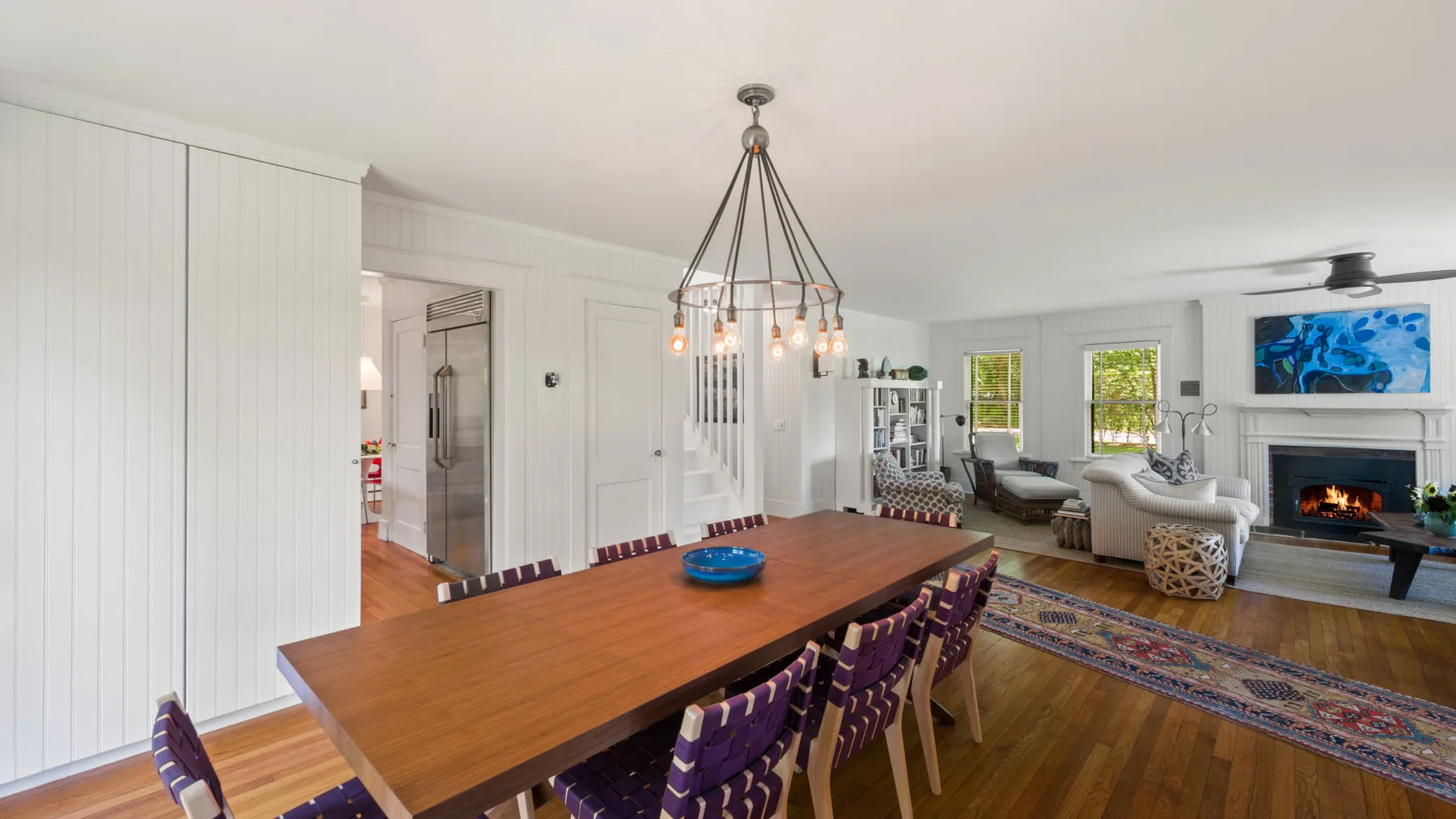 A bright dining and living room with a long wooden table and a fireplace.