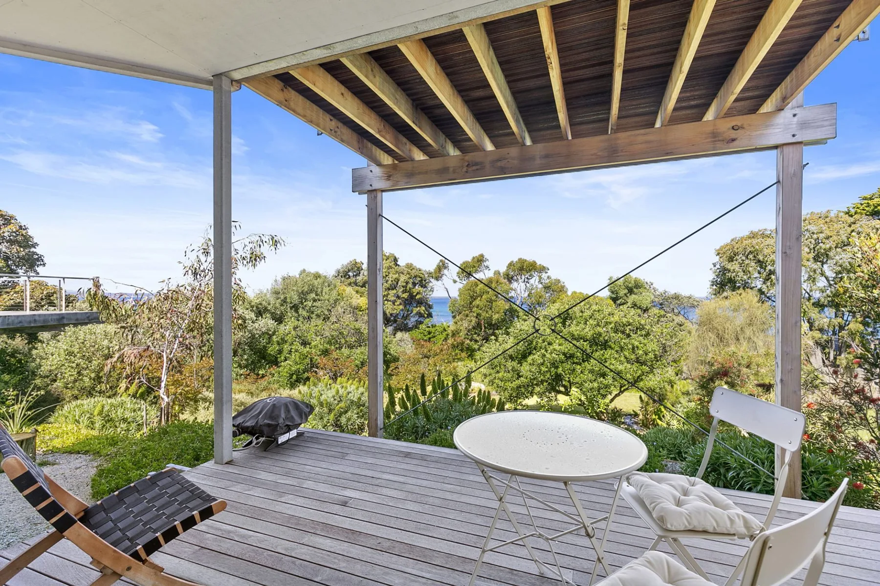 Una terraza de madera cubierta da a un jardín con árboles y vegetación.