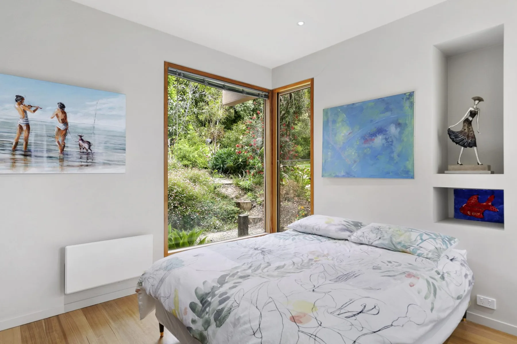 Dormitorio con una cama junto a una puerta de vidrio abierta que da a la vegetación.