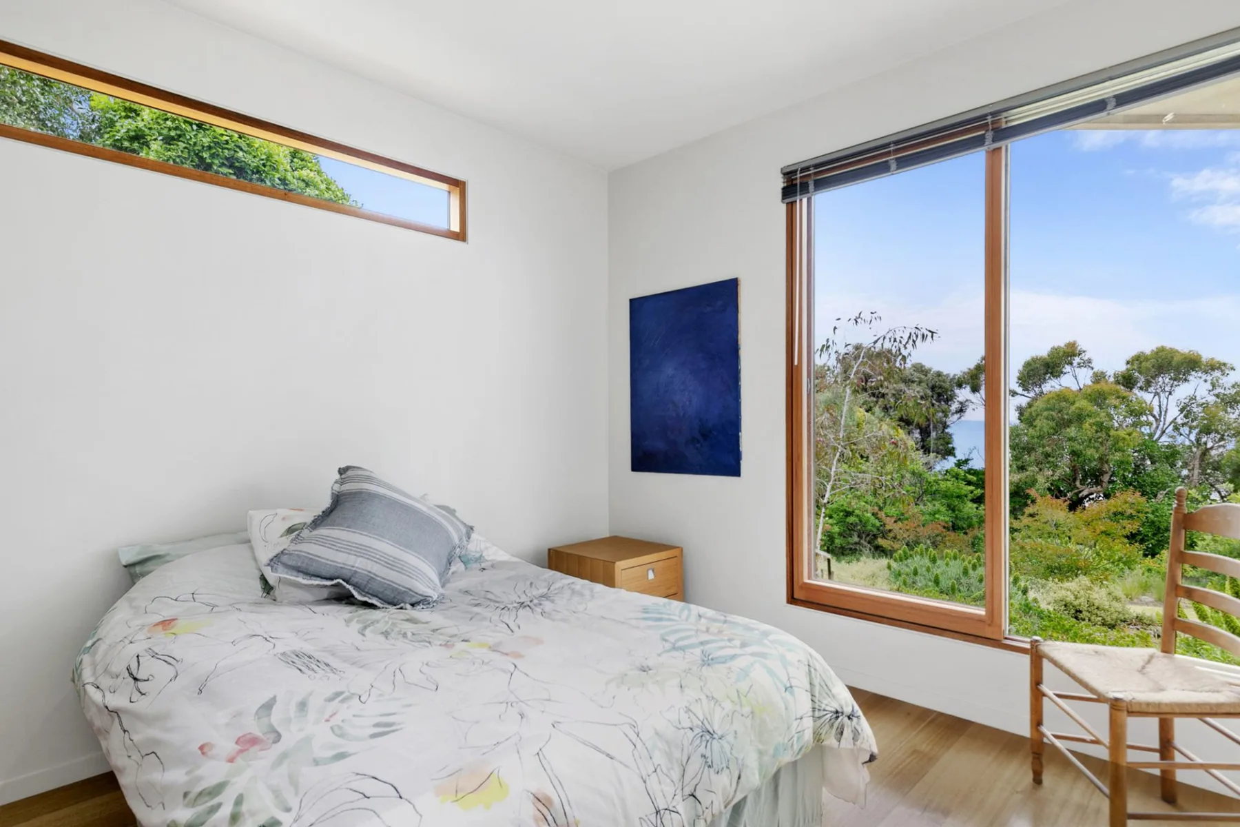 Dormitorio con una cama junto a una ventana grande con vistas a la vegetación.