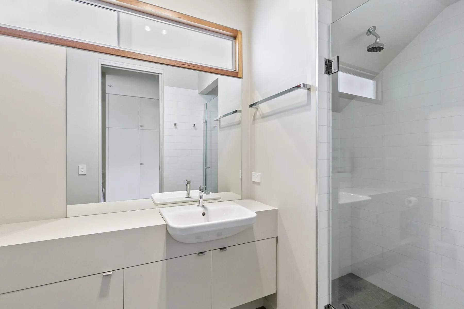 Un baño luminoso con lavabo, espejo amplio y ducha de vidrio.