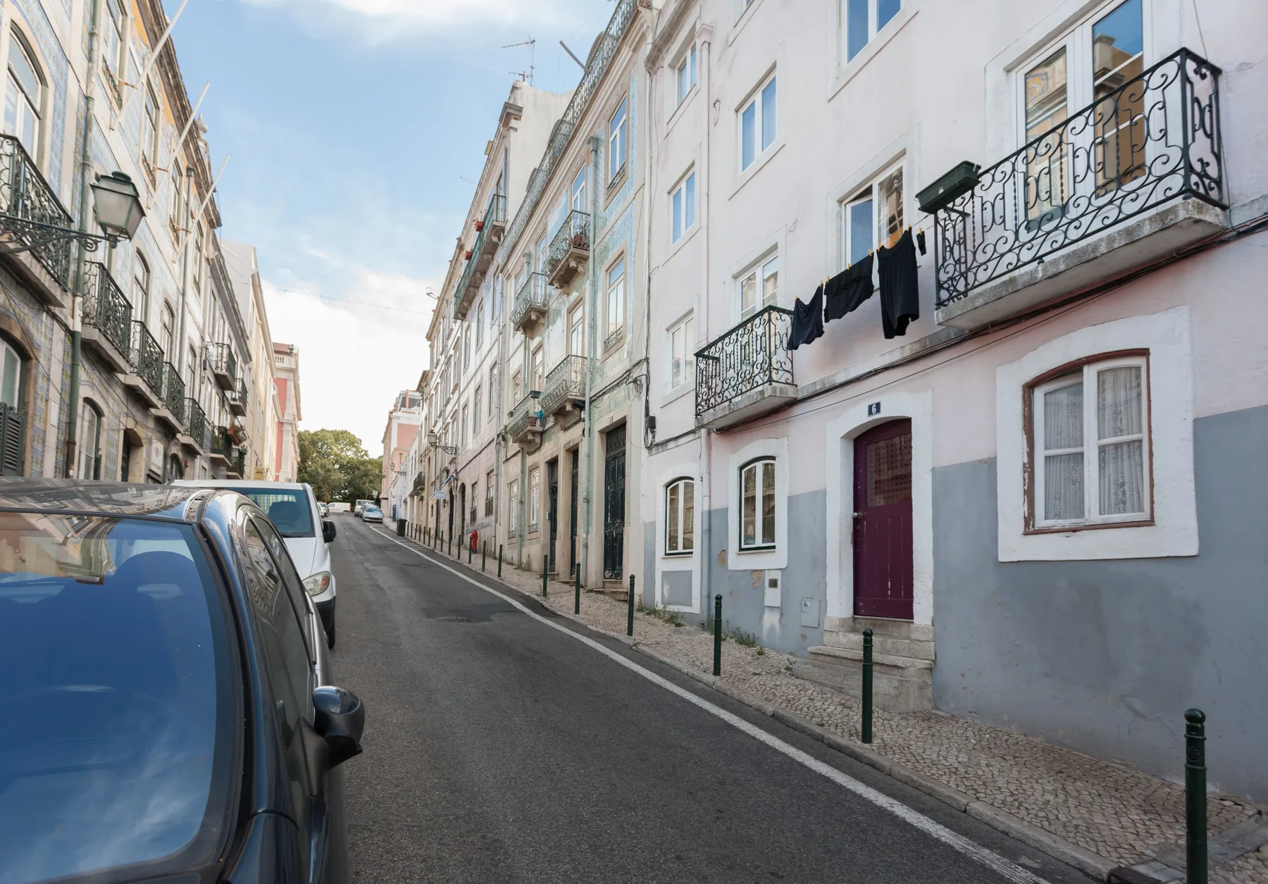 Una calle residencial estrecha flanqueada por edificios de varias plantas y coches aparcados.