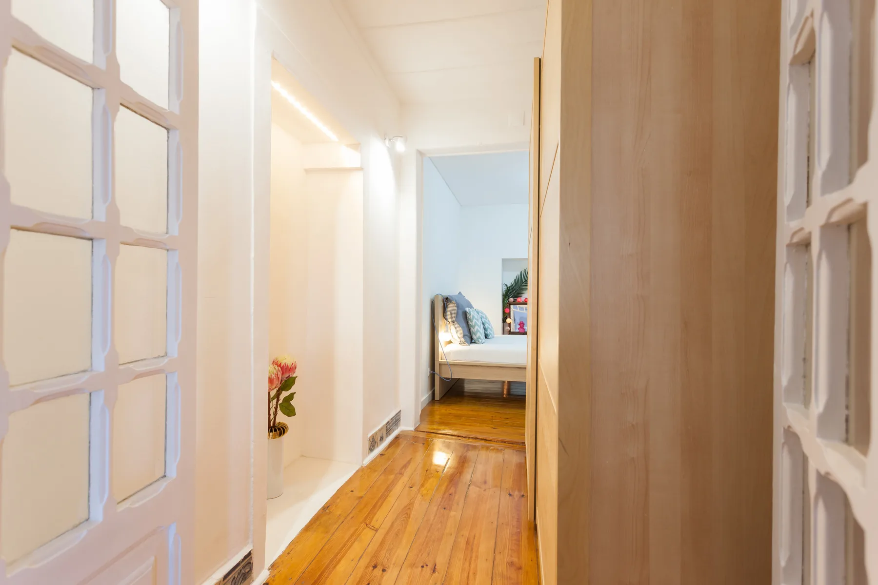 Un pasillo luminoso con suelo de madera conduce a un dormitorio.