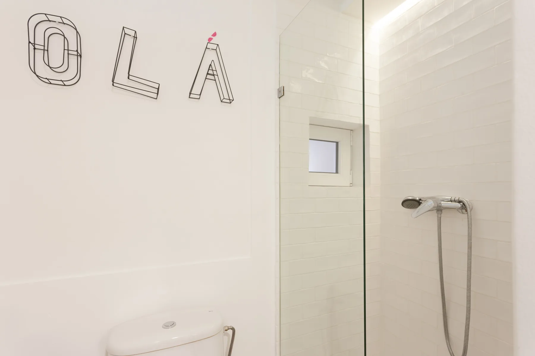 Un baño alicatado con una mampara de vidrio y una ducha fijada a la pared.