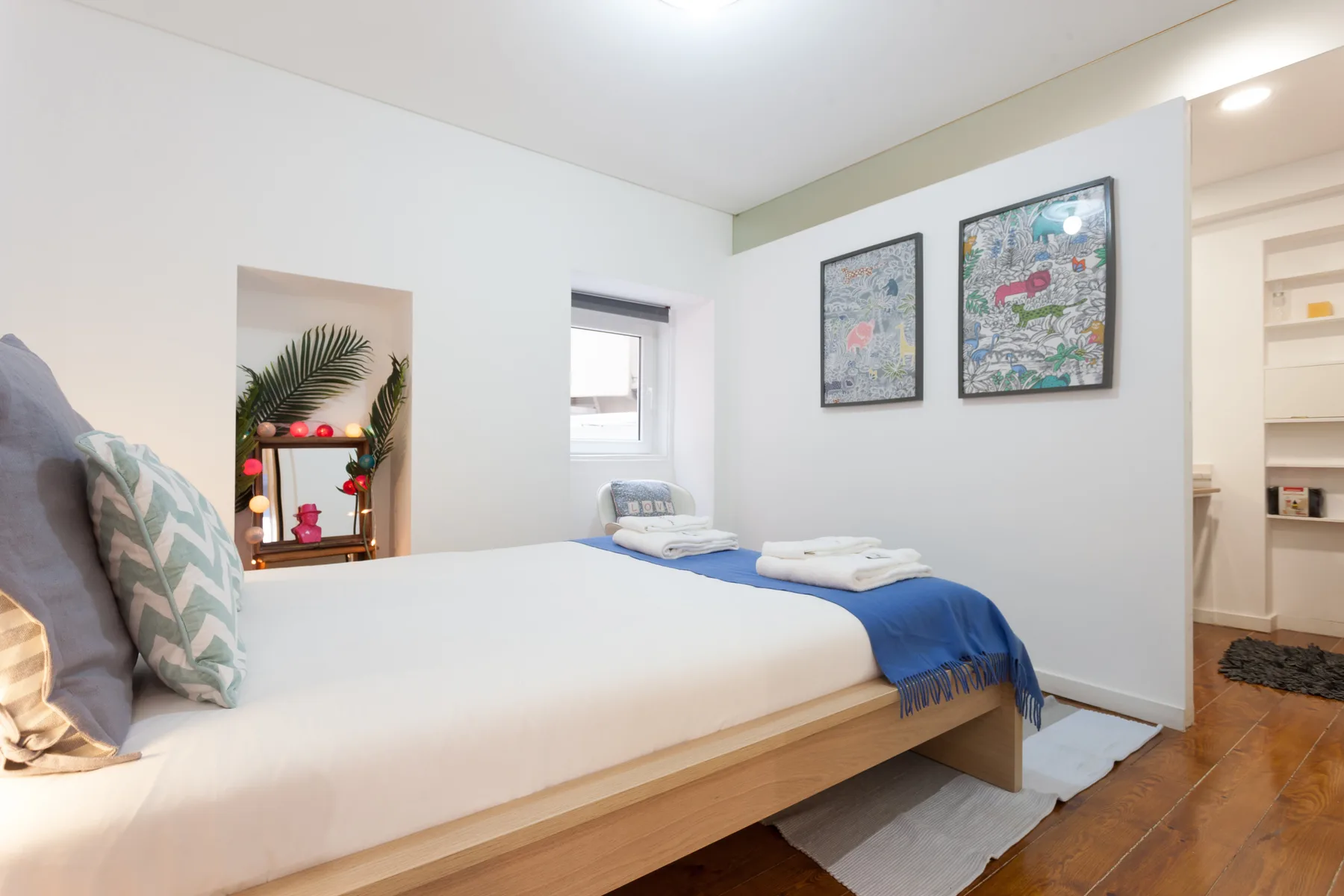 Dormitorio con una cama, cuadros coloridos y estanterías empotradas.