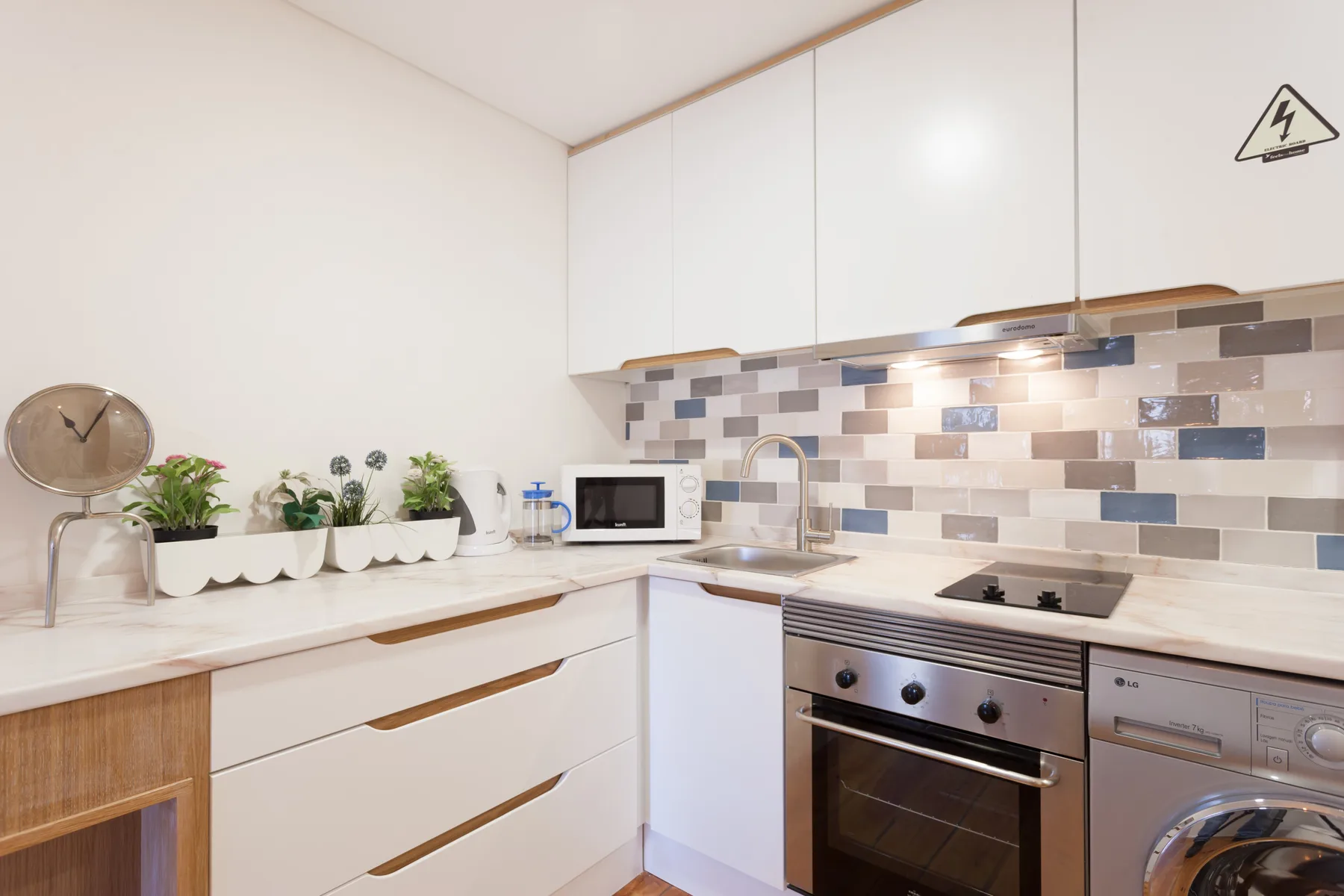 Una cocina luminosa con armarios blancos, un salpicadero de azulejos y un horno integrado.
