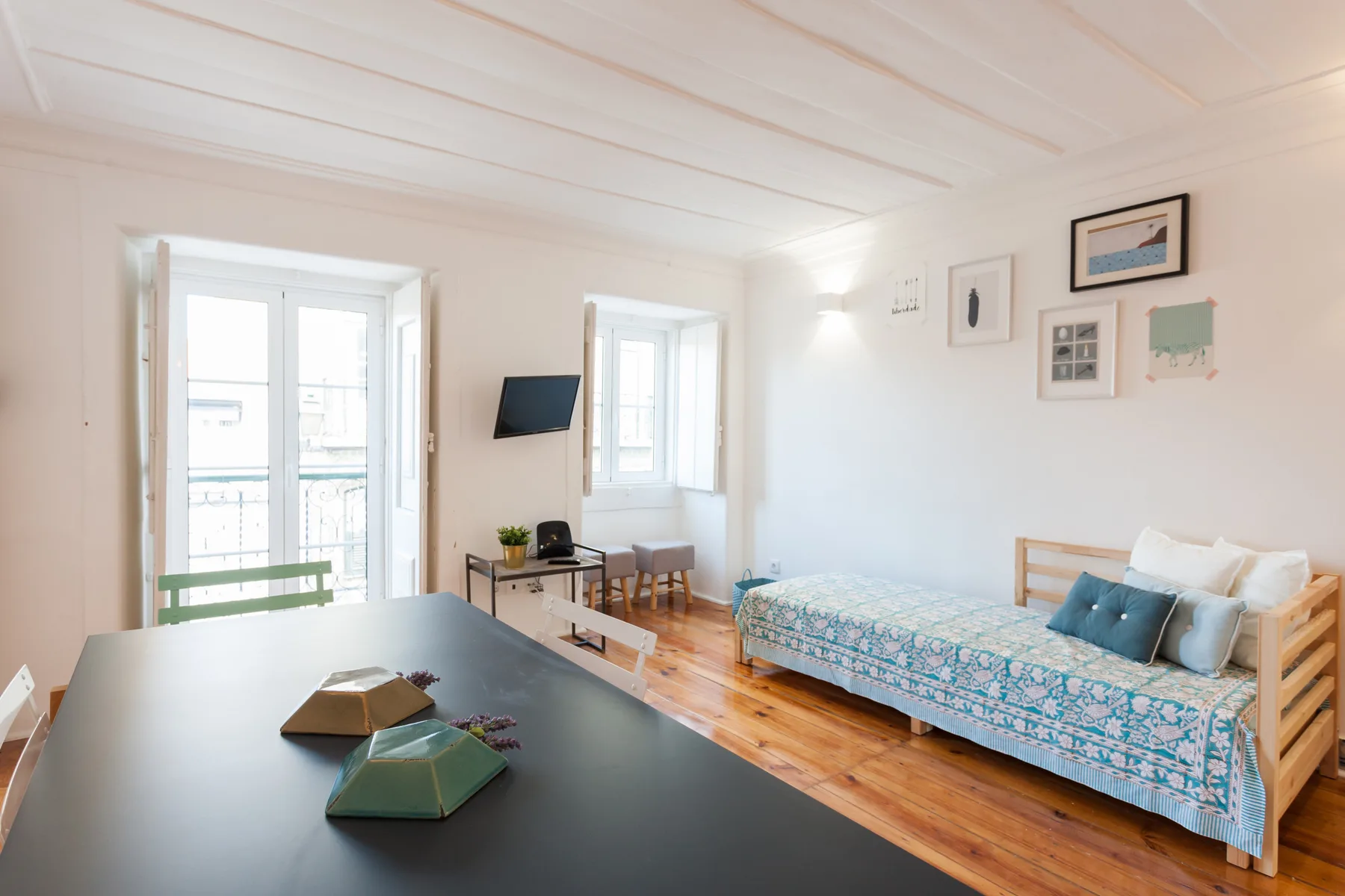 Un salón luminoso con una cama de día, una mesa y ventanas altas.