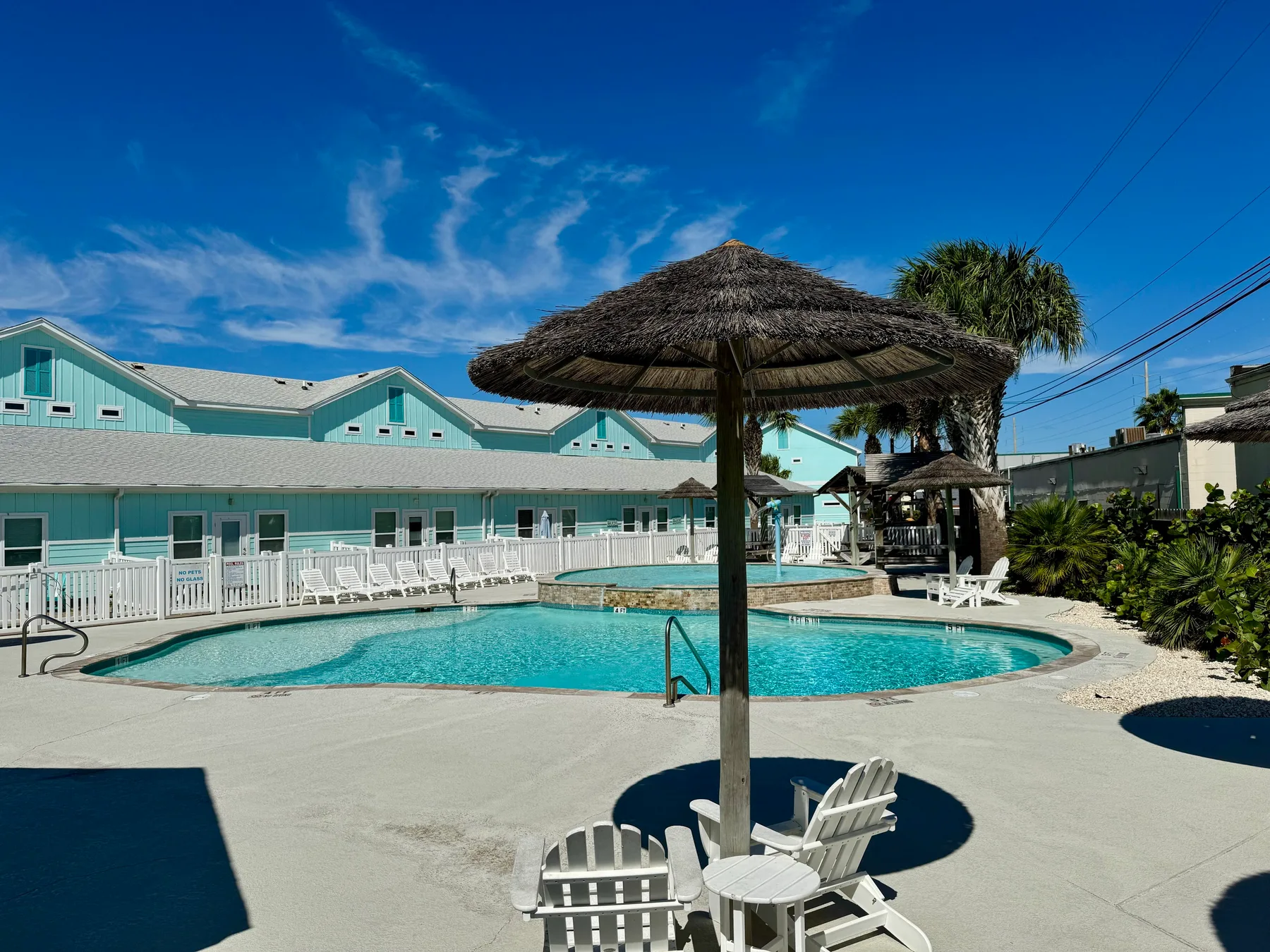 An outdoor swimming pool with a thatched shade umbrella and white seating.
