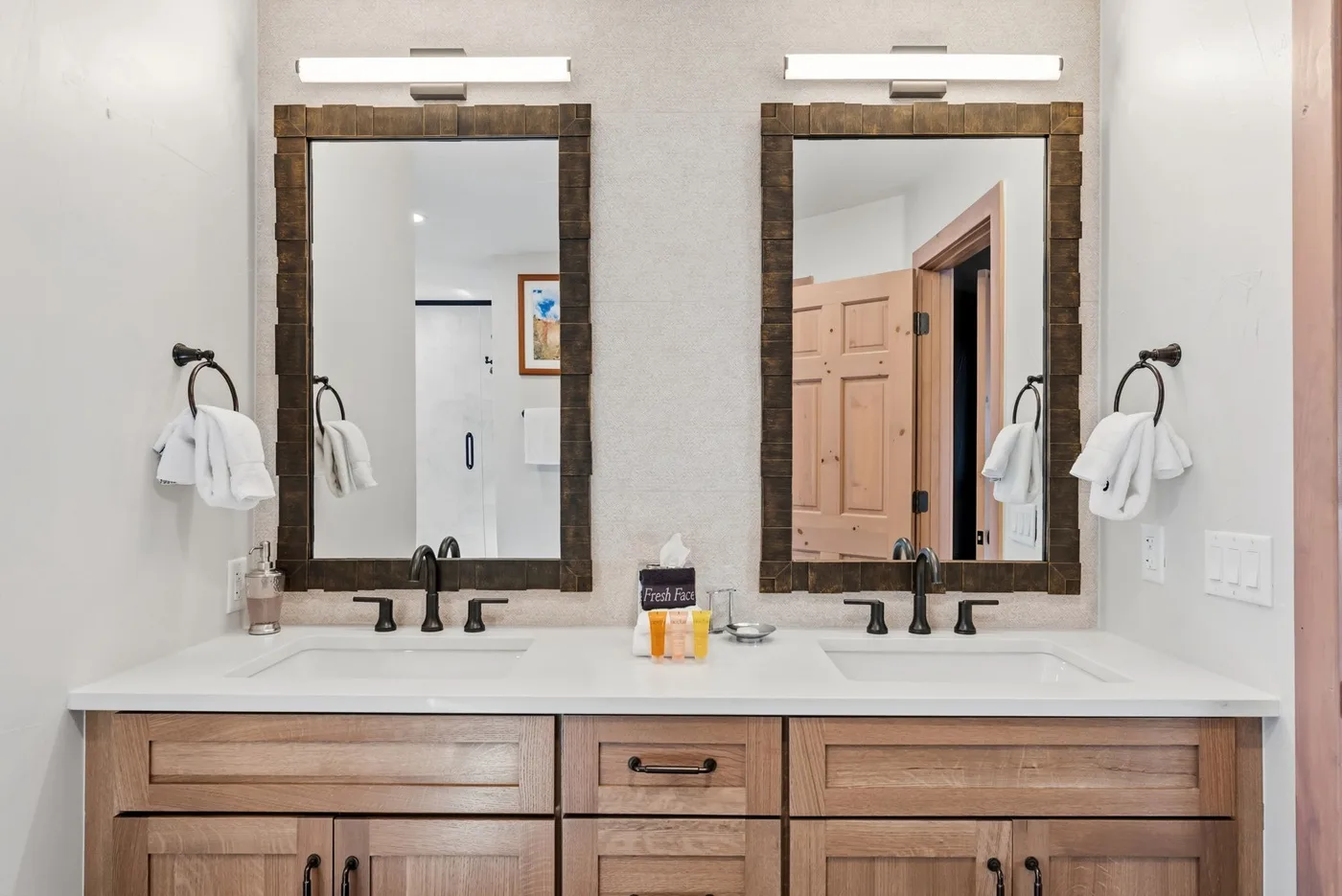 Un tocador de baño con dos lavabos, espejos enmarcados y luces de pared.