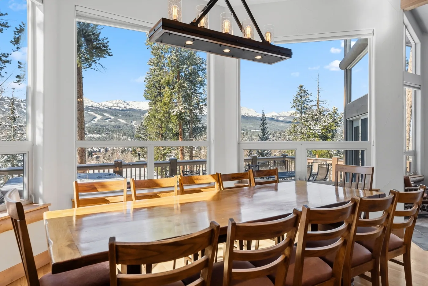 Comedor con una larga mesa de madera y grandes ventanas con vistas a un paisaje montañoso.