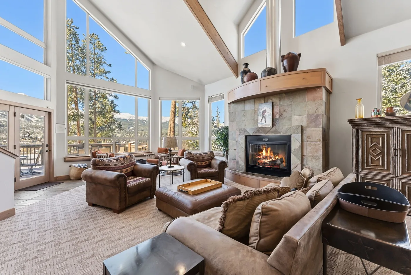 Una sala luminosa con asientos alrededor de una chimenea y grandes ventanas.