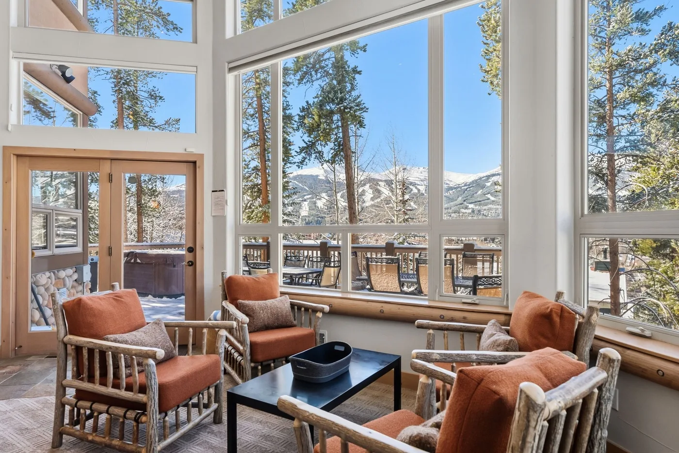 Una sala de estar luminosa con grandes ventanas que dan a un paisaje montañoso nevado.